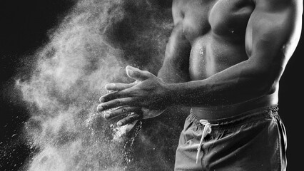 Fototapeta na wymiar A man claps his hands, creating a cloud of chalk dust, against a black background.