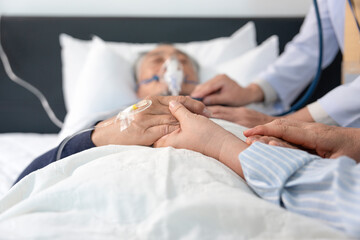 scene of a wife holding hands hopeless senior male patient who have oxygen and intravascular...
