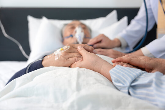 scene of a wife holding hands hopeless senior male patient who have oxygen and intravascular solution drip lying on bed,doctor examining a dying patient,concept of palliative care,end of life care