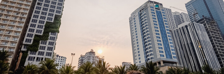 Sunset over modern skyscrapers with lush greenery, highlighting urban development and environmental sustainability in a tropical city