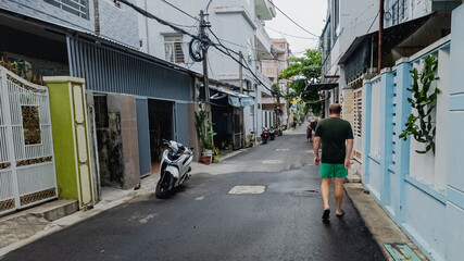 Fototapeta premium A man walks down a narrow residential street in Vietnam, highlighting everyday urban life and travel experiences in Southeast Asia