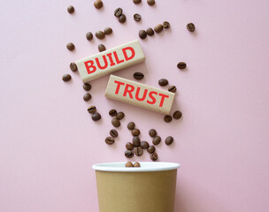 Build trust symbol. Wooden blocks with words Build trust. Beautiful pink background with coffee...