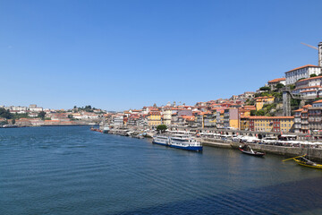 Obraz premium Picturesque view of the Ribeira district in Porto, with traditional colorful houses along the Douro River and boats docked at the dock under a blue sky. Porto - Portugal