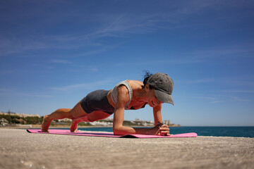 Brunette Woman Performing Isometric Exercises on Pink Exercise Mat by the Sea