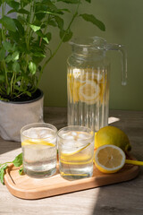 Summer lemonade beverage in glasses and jug on table in bright sunlight with shadows, lifestyle food still life