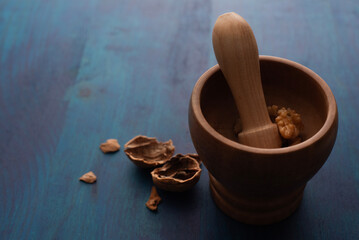 Comida. Nuez Chandler rota, dentro de mortero de madera con cascaras fuera, sobre mesa azul de madera.