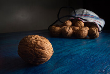 Comida. Nuez Chandler separada de una pequeña bolsa llena de nueces sobre mesa azul.