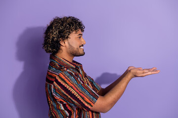 Side profile photo of nice man with beard dressed print shirt arms presenting object look empty space isolated on purple color background