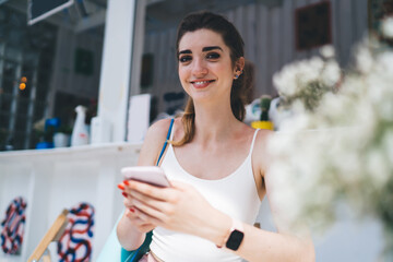 young woman enjoys moment of relaxation at outdoor café, smiling warmly while engaging with smartphone and online shopping. modern, connected lifestyle, combining recreation and technology seamlessly