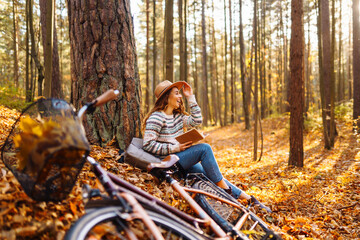 Beautiful smiling young woman student sitting and reading book at autumn park fall yellow foliage leaves. Concept of enjoying nature.
