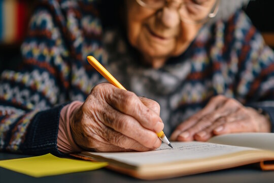 Elderly woman with glasses writing in notebook with yellow pen. Concept for reflection, memory keeping, and Alzheimer's awareness - Powered by Adobe