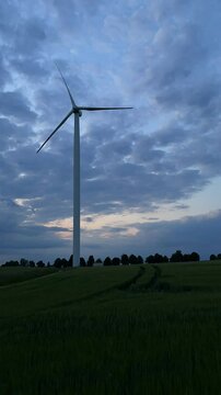 Time-lapse of a single wind turbine in a rye field over the sunset sky. Windmill blades generate green energy. Concept of a clean electricity production preventing climate change. 