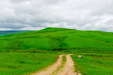 Obraz premium A dirt road leading to a green picturesque hill. Caucasus