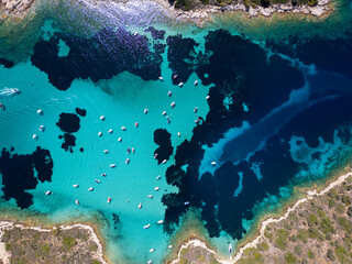 Aerial view of a turquoise lagoon with numerous boats floating on clear water, surrounded by dark...