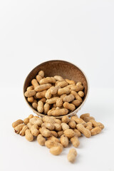 Bowl of Dry Roasted Peanuts Spilled on a White Background