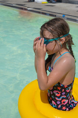 A girl with wet hair puts on goggles for diving in the pool
