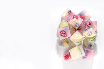 Infused fruit gin tonic ice cubes for iced summer cocktail and drinks, assorted homemade various ice cubes with berries, lemon, cucumber, lime  on white background copy space
