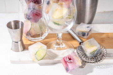 Infused fruit gin tonic ice cubes for iced summer cocktail and drinks, assorted homemade various ice cubes with berries, lemon, cucumber, lime  on white background copy space