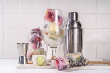 Infused fruit gin tonic ice cubes for iced summer cocktail and drinks, assorted homemade various ice cubes with berries, lemon, cucumber, lime  on white background copy space