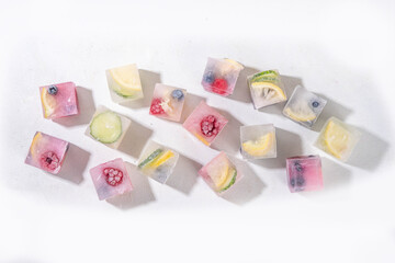Infused fruit gin tonic ice cubes for iced summer cocktail and drinks, assorted homemade various ice cubes with berries, lemon, cucumber, lime  on white background copy space