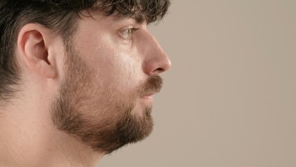 Obraz premium Handsome bearded male model posing at camera. Young adult man isolated on white background, close up shot. Natural beauty skin care concept. Side view.