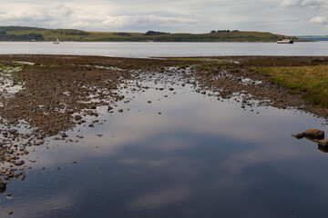 A view from the seaside town of Largs, showing the Scottish coast, where a ferry makes its way to the island of Cumbrae, set against the backdrop of a beautiful summer's day.
