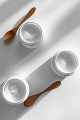 The beauty of skincare, two white cream jars with wooden spoons, minimalistic composition in natural light, moisturizing product, skincare concept