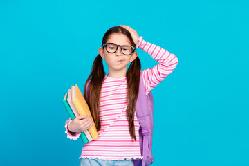 Photo of upset girl dressed striped shirt backpack on shoulder in glasses hold book palm on head isolated on blue color background