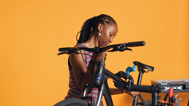 BIPOC mechanic setting up bike repair stand, using it to adjust handlebar and fix broken wheels, studio background. Professional placing bicycle on workstand in tight grip to inspect it, camera A