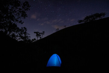 View of the center of the milky way with a blue illuminated camping tent