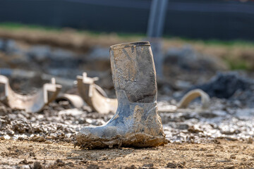 Close-up of a single dirty, muddy, rubber work boot on a construction site.
