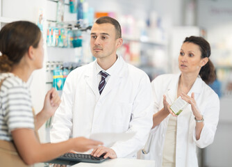 Kind male druggist and his female assistant choosing medicine for client showing recipe sheet in chemist's shop