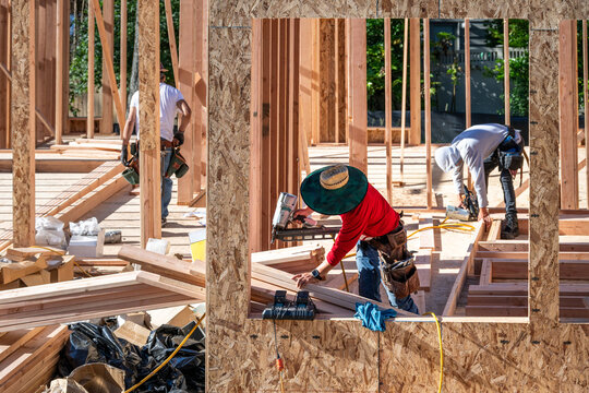 Construction work crew building a new house in a residential neighborhood, wood framing started, sunny summer construction season
