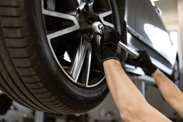 Mechanic performing tire maintenance using tools in auto repair shop. Close-up of gloved hands...