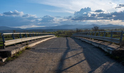 Overpass over the highway. In the distance stretches a beautiful blue sky dotted with white clouds.
