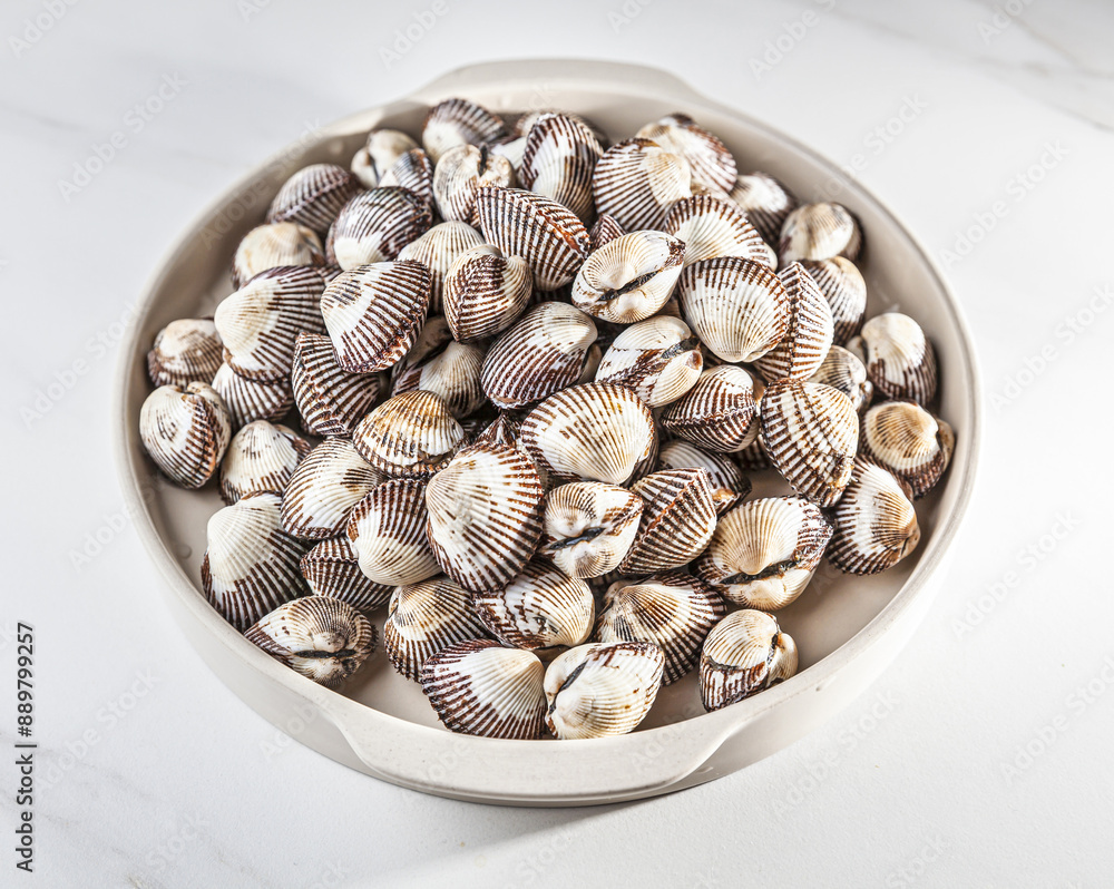 Wall mural Close up of stacked raw cockles on bowl and white floor, South Korea
