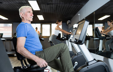 Elderly athletic man in sportswear training on exercise bike in gym