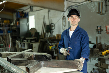 Male welder standing with a welding semi-automatic machine and a safety helmet in a metal machining...