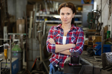 Female employee of workshop stands next to vise, resting from labors. Woman takes break during...