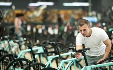 Interested avid cyclist choosing new bike for cycling trips in busy store, carefully picking...