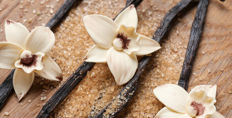 Aromatic vanilla sugar, flowers and sticks on wooden background