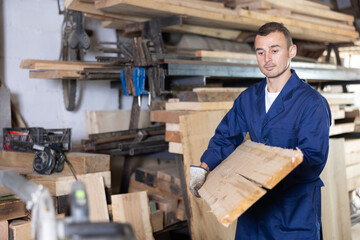Male sawmill worker stores wooden boards in the enterprise warehouse
