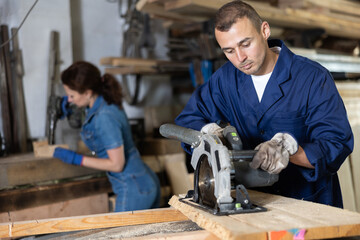 Young man worker saws oak plank with electric saw in oak workshop
