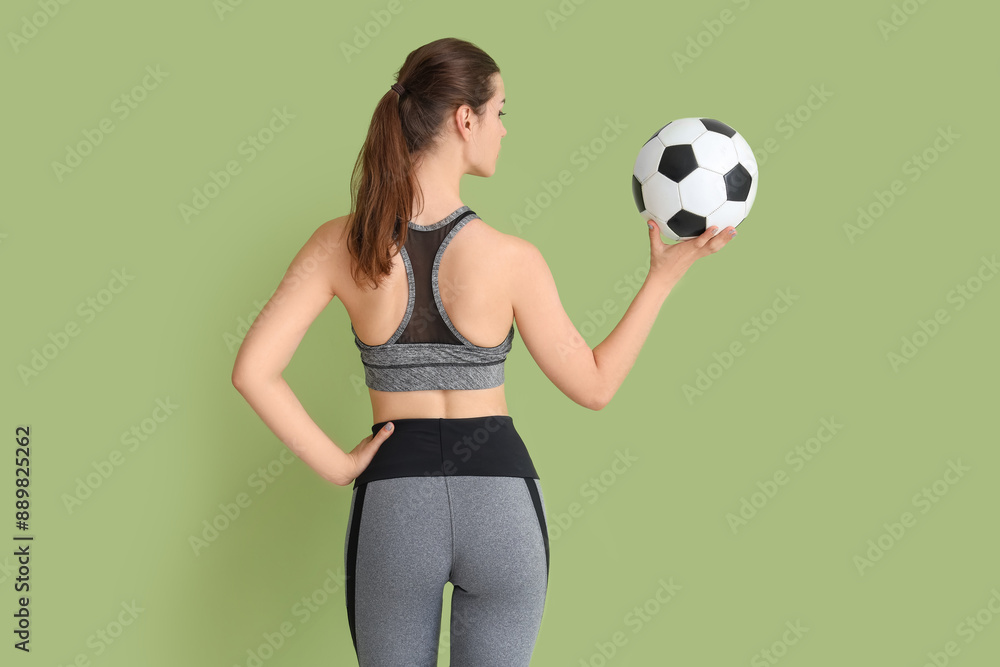 Wall mural Sporty young woman with soccer ball on green background, back view