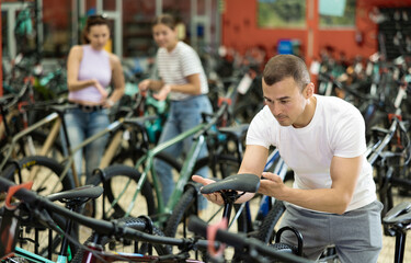 Fototapeta premium Attentive young guy choosing model seat on high-speed bike in modern sports shop