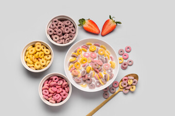 Bowls of colorful sweet cereal rings with milk and cut strawberry on grey background