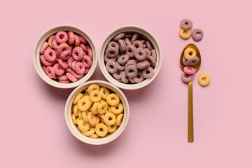 Bowls and spoon with colorful sweet cereal rings on pink background