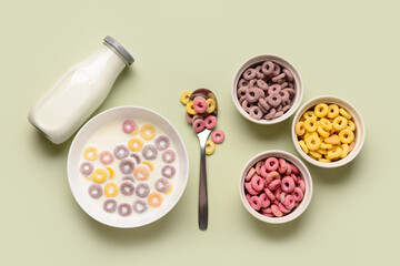 Bowls of colorful sweet cereal rings with milk on green background