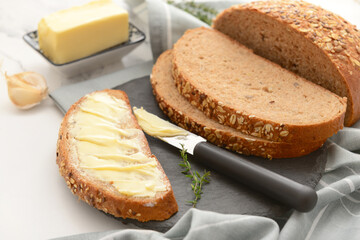 Black board of bread slices with fresh butter and garlic on white background