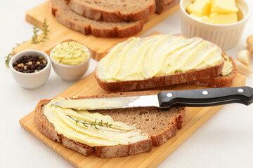 Wooden board of bread slices with fresh butter and bowl of peppercorn on white background